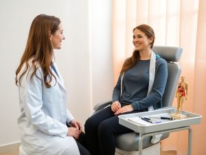 Ginecologă cu halat alb și pacientă zâmbitoare în cabinet luminos.