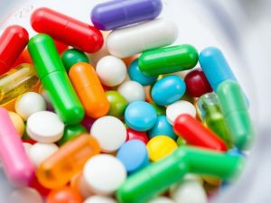 Pastile colorate si capsule intr-un recipient transparent.